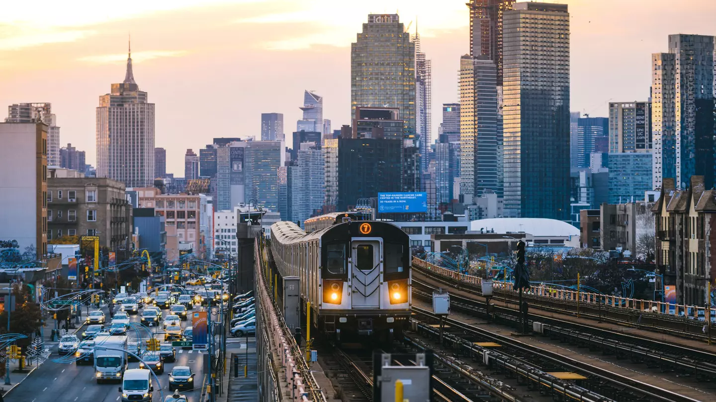 A train runs along an elevated railway line beside traffic in Queens, New York City, USA.