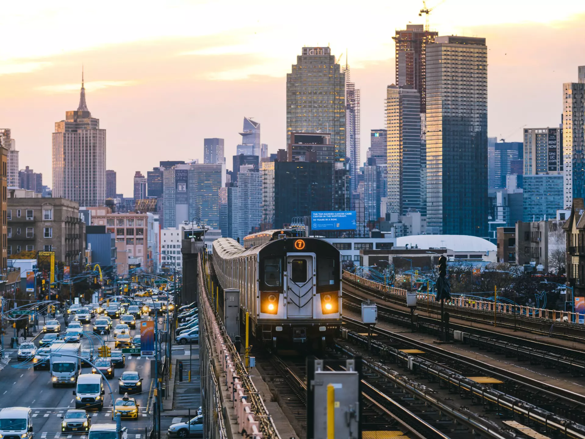A train runs along an elevated railway line beside traffic in Queens, New York City, USA.