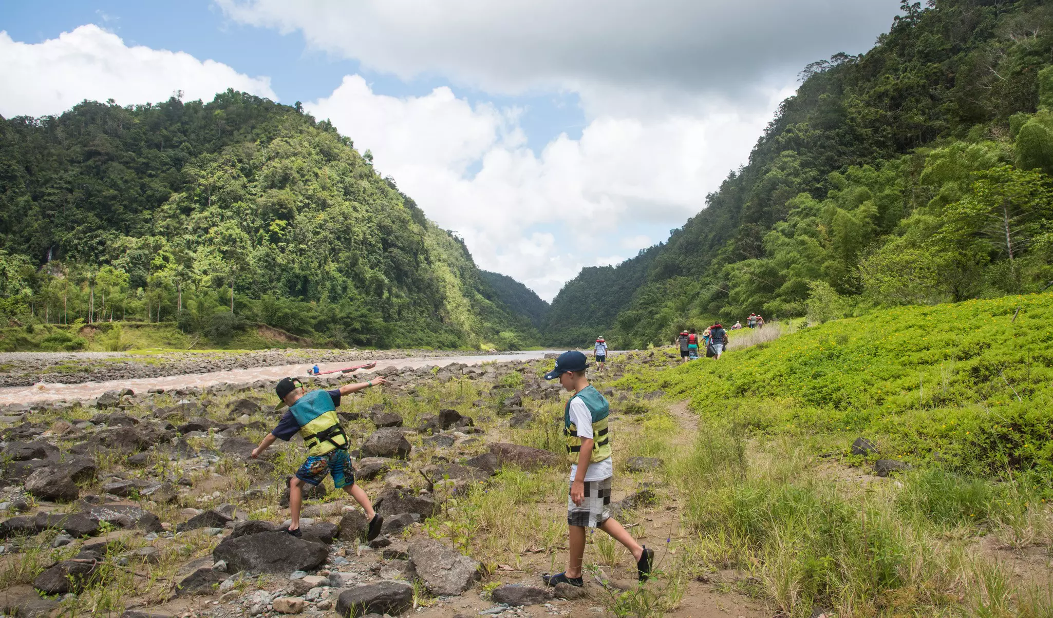 Tourists hiking Navua River rocky bank with rainforest in Suva, Fiji/Rocky Riverbank Hike