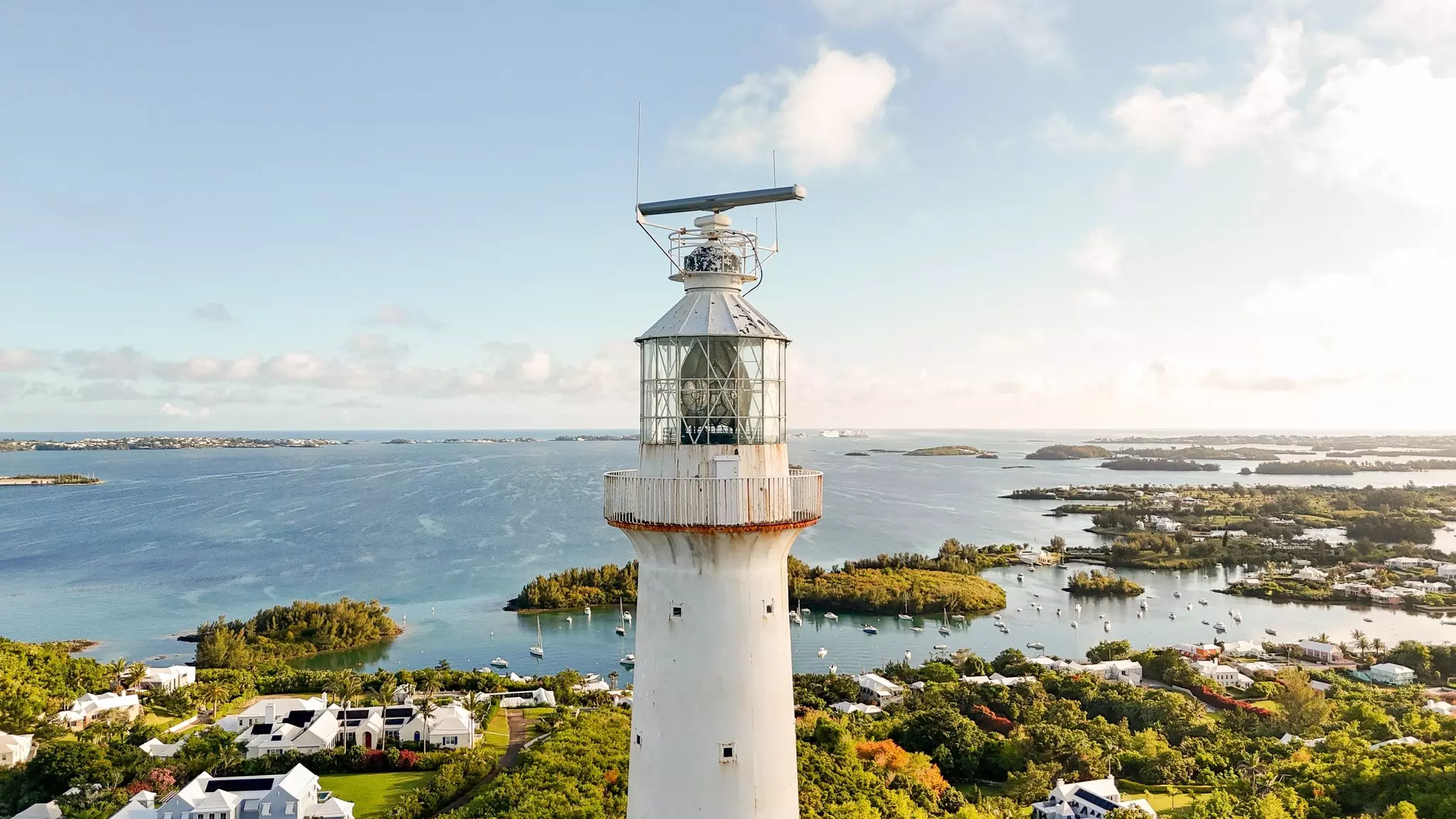 An aerial view of the tower of a lighthouse with buildings and the ocean beyond.