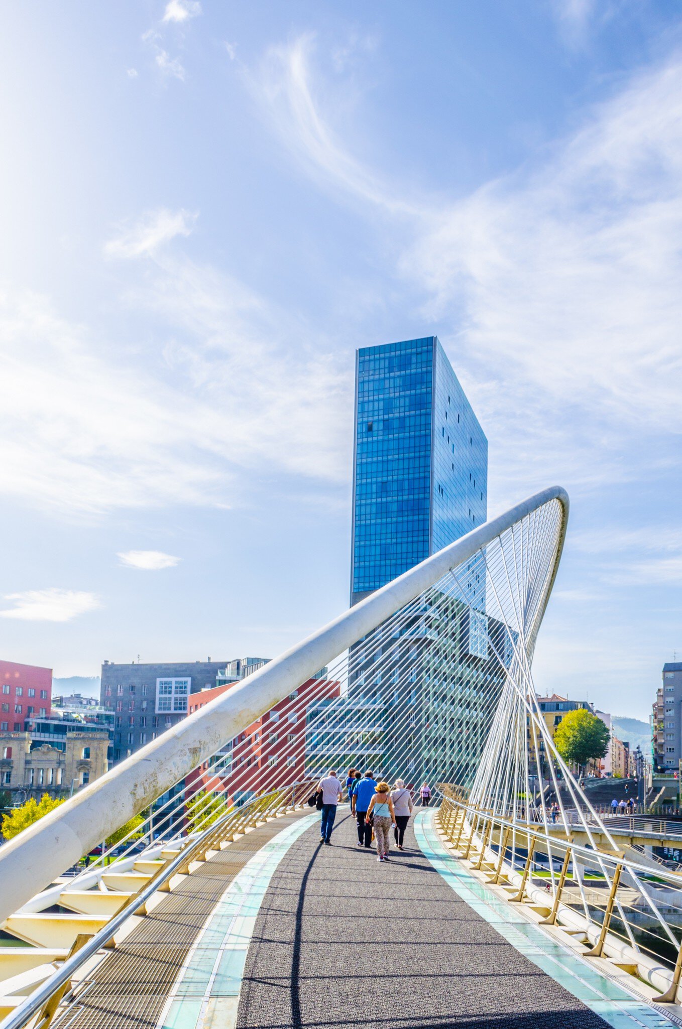 People crossing the Zubizuri bridge on a sunny day in Bilbao, Spain.