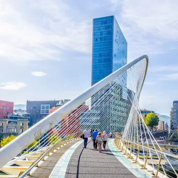 People crossing the Zubizuri bridge on a sunny day in Bilbao, Spain.