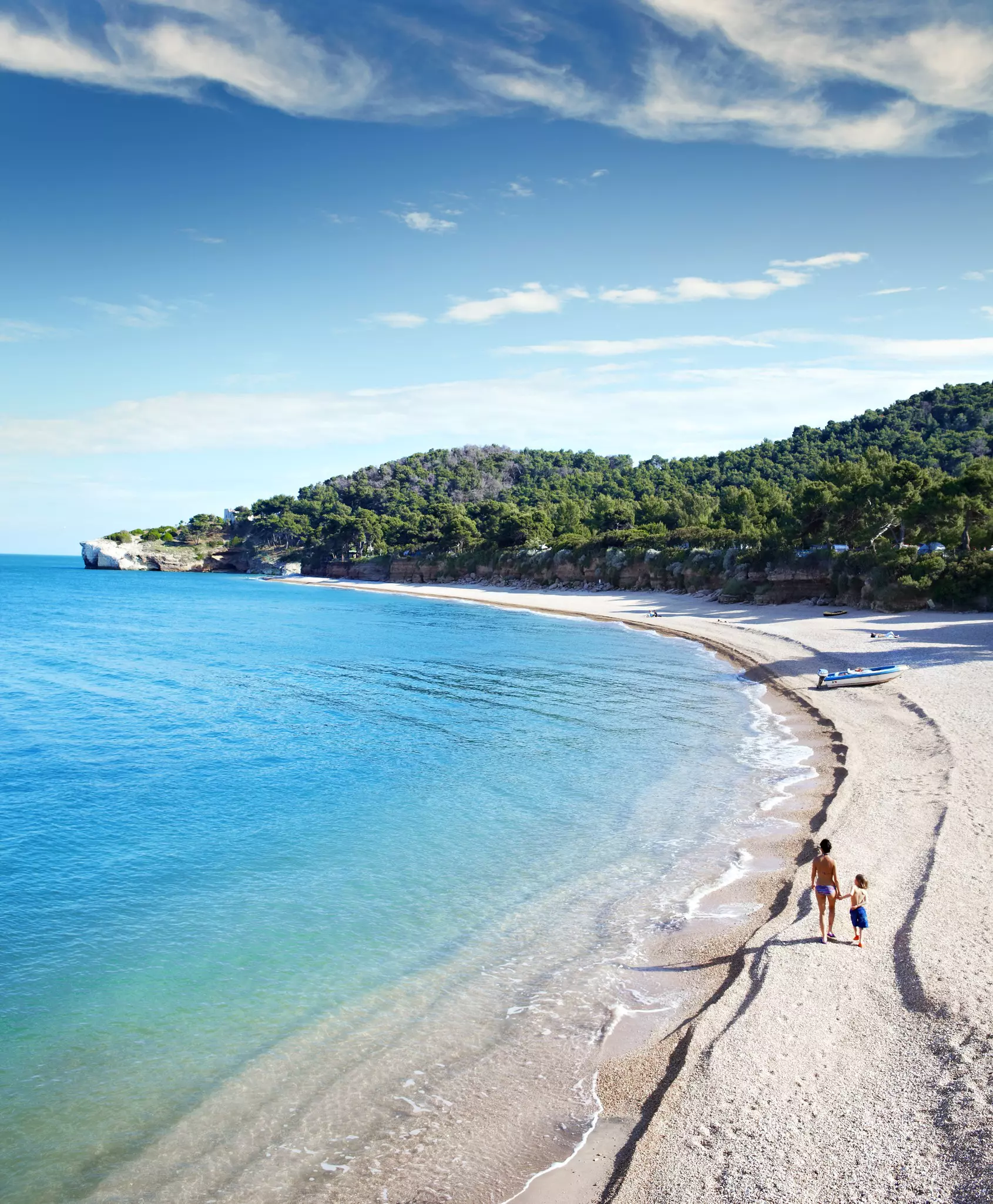 Woman and child walking on a beach with bright blue water