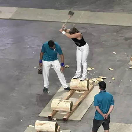Woman using axe to chop log she is standing on