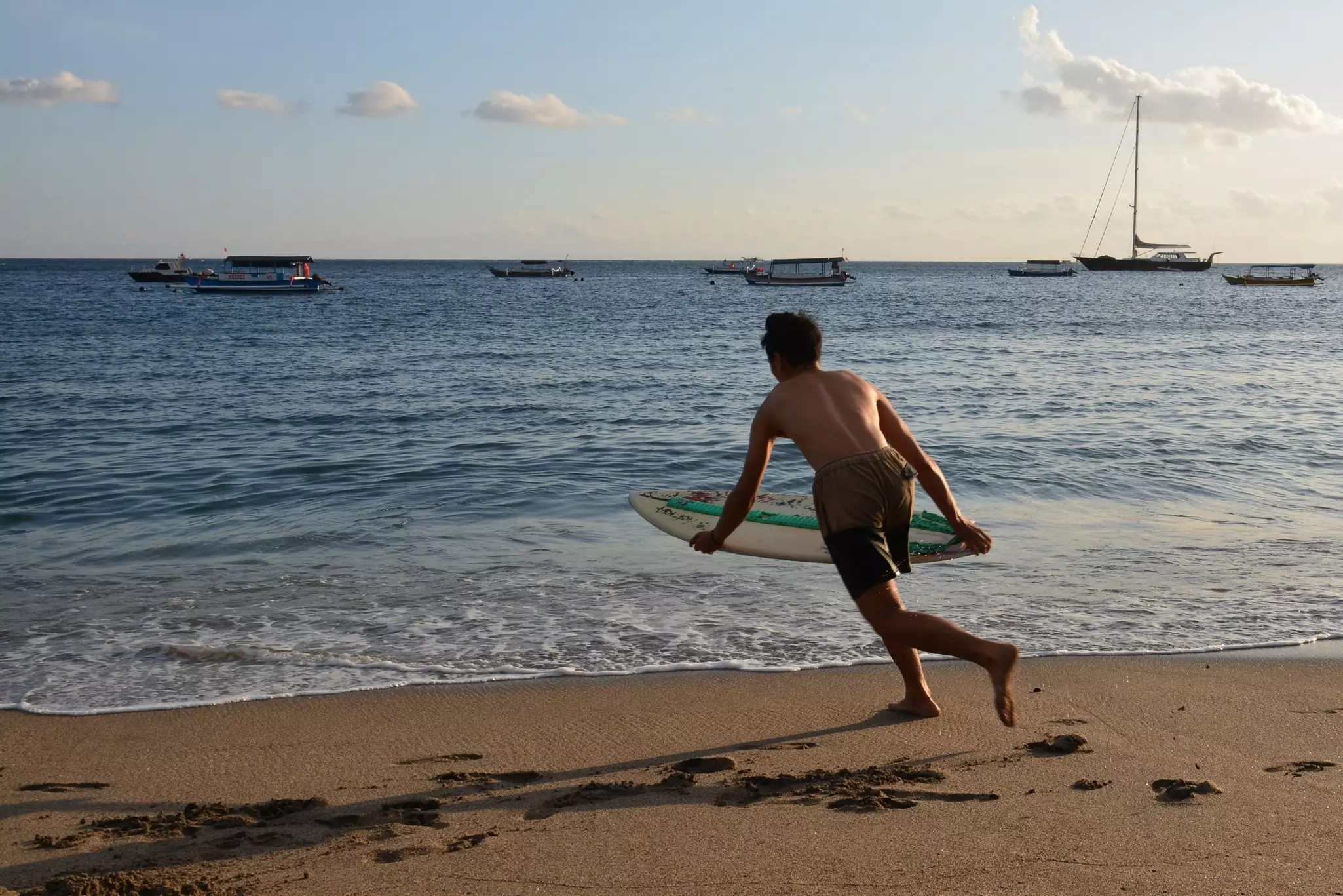 A surfer holding his board runs toward the waves on a beach.