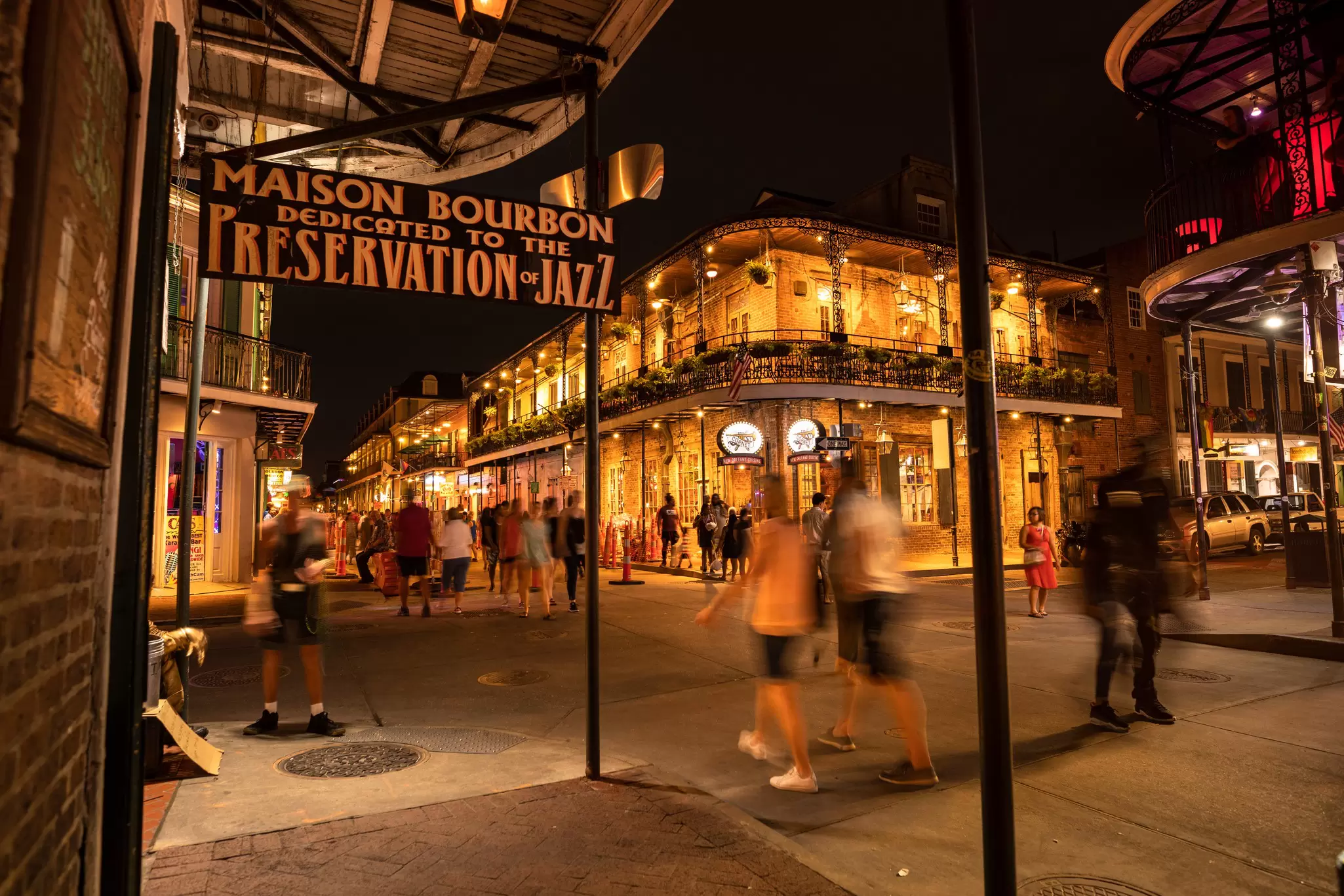 People walk past historic building with wrought-iron facades and balconies by night, the French Quarter, New Orleans.