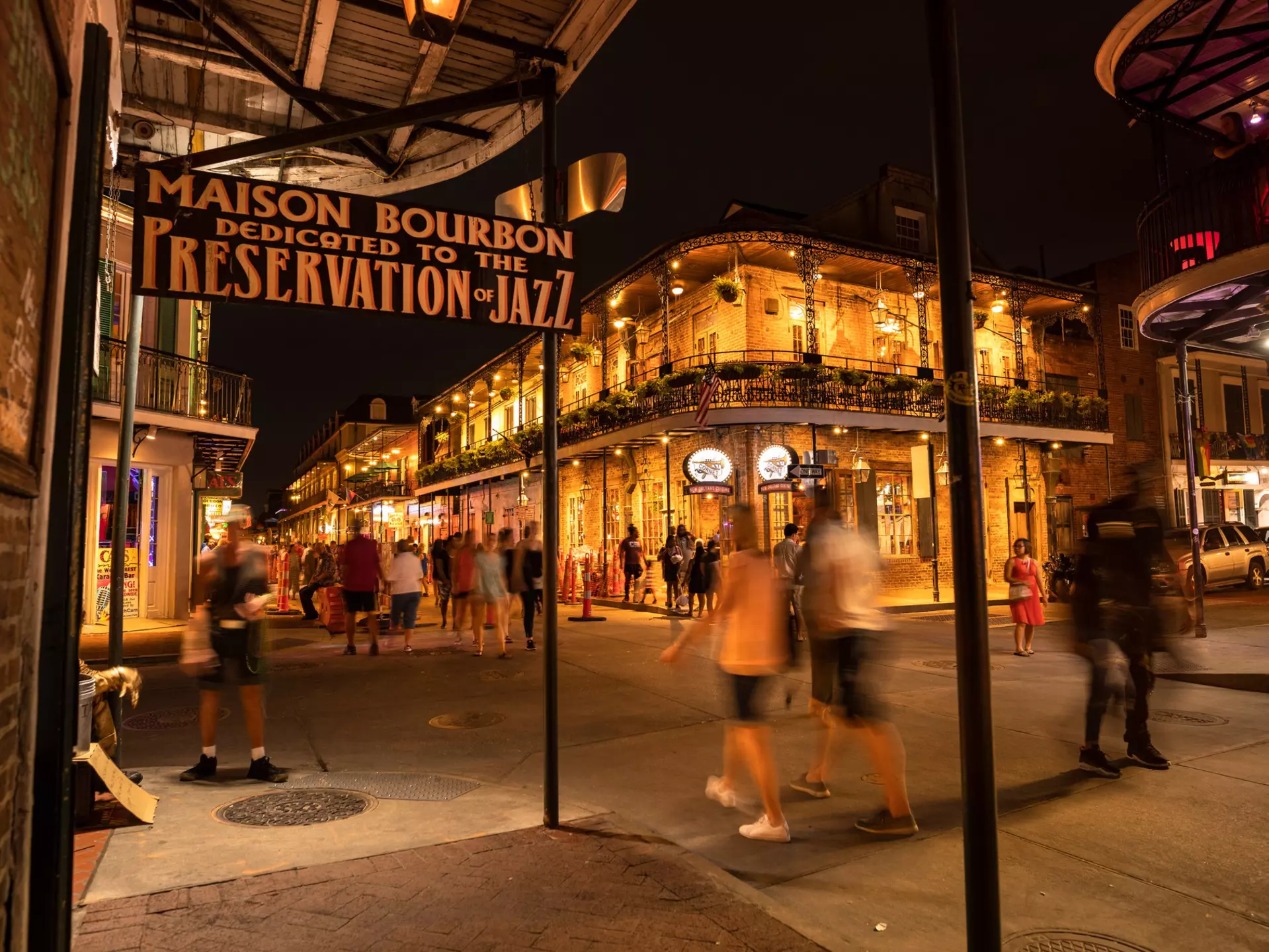 People walk past historic building with wrought-iron facades and balconies by night, the French Quarter, New Orleans.