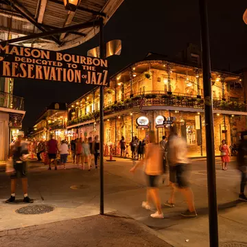People walk past historic building with wrought-iron facades and balconies by night, the French Quarter, New Orleans.