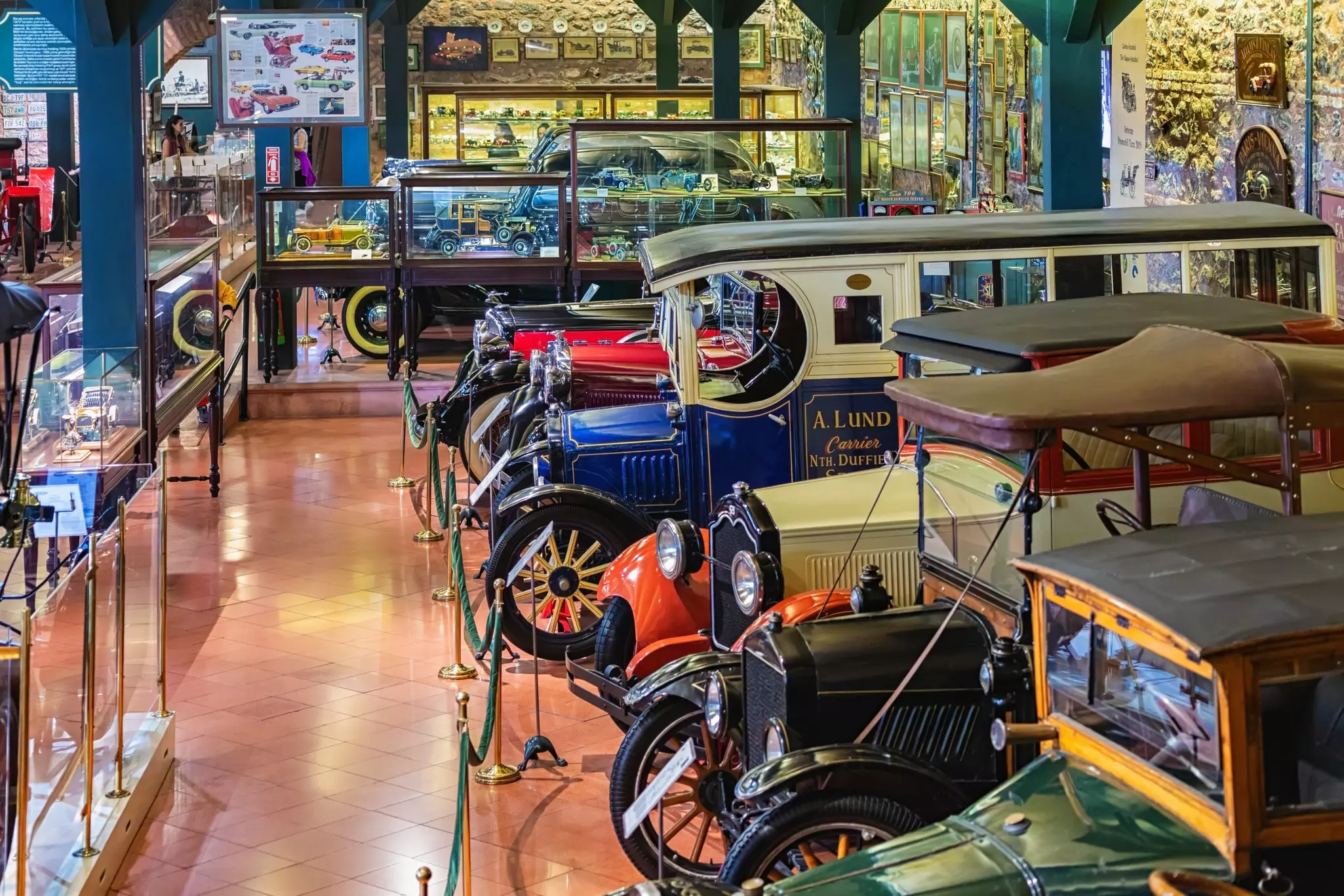 A museum room with transport-related displays around the outside and six old-fashioned motorcars parked in a line
