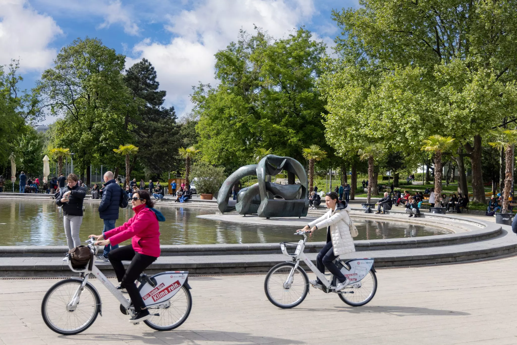 : People ride bikes and relax in the park in the Karlsplatz in front of Church of St. Charles (Karlskirche)