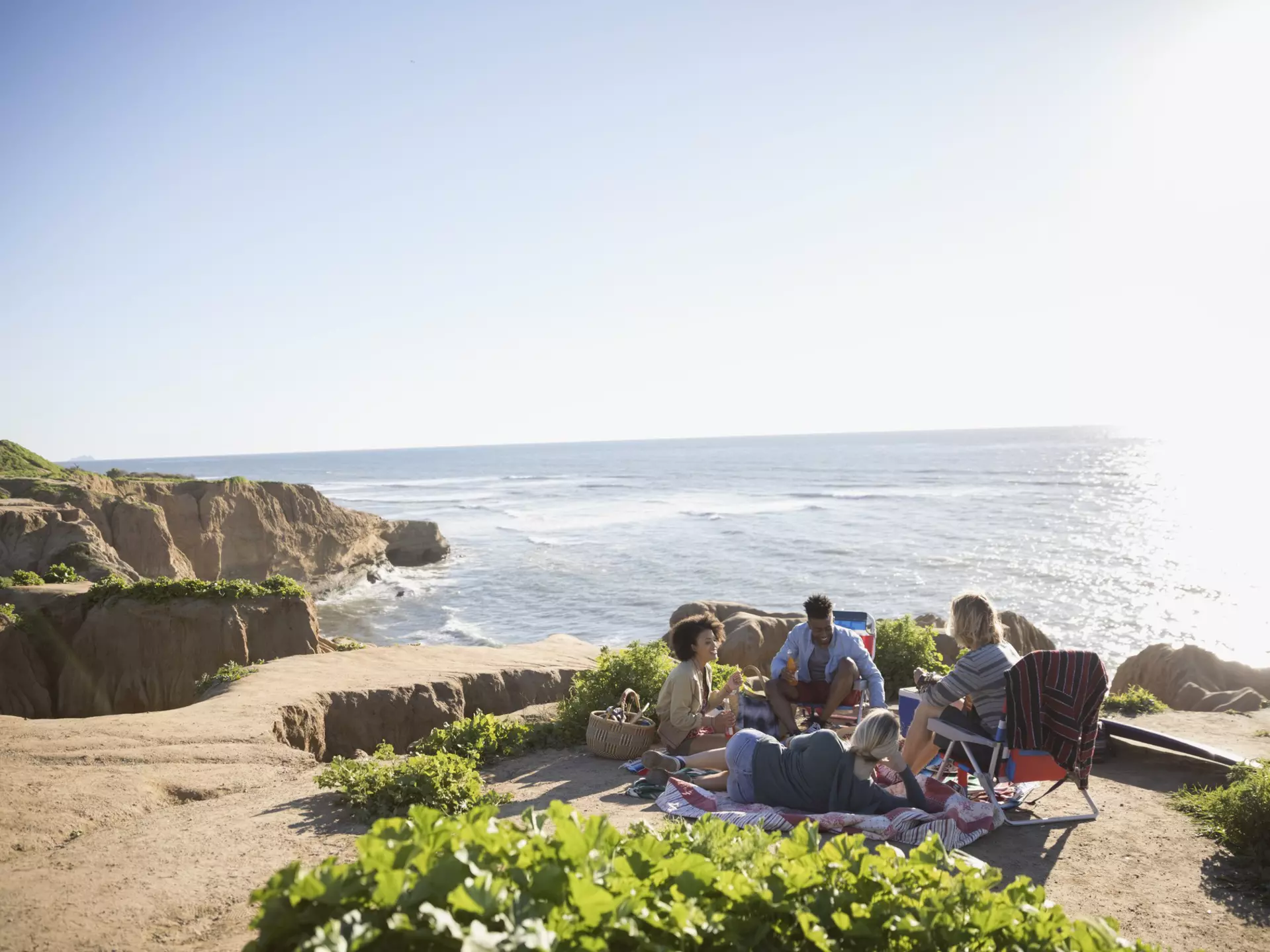 Young friends hanging out on a sunny clifftop with the ocean beyond.