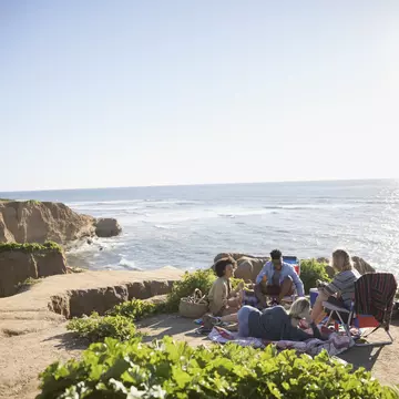Young friends hanging out on a sunny clifftop with the ocean beyond.