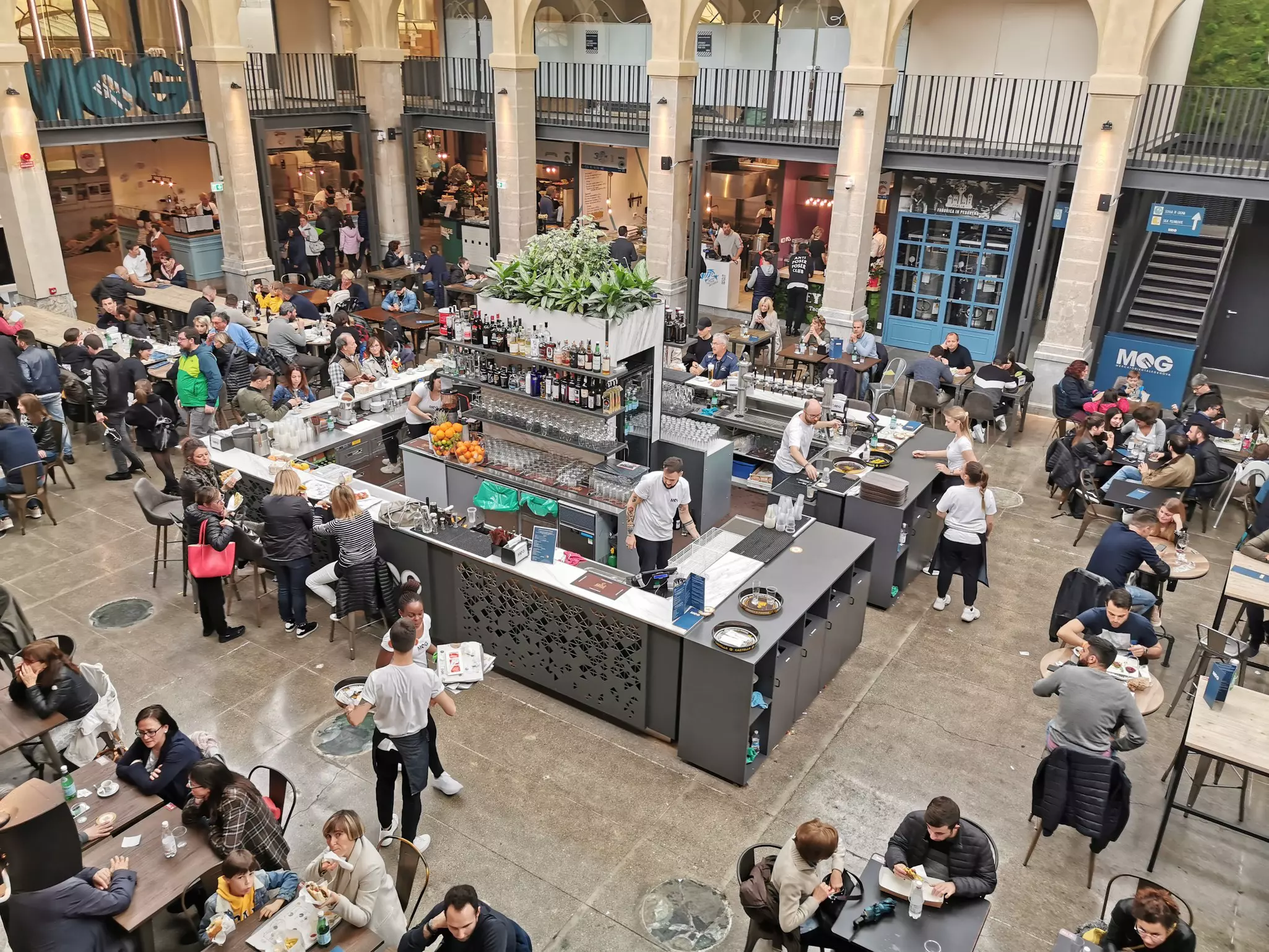 An overhead view of the atrium of a lively city market filled with tables and stalls.