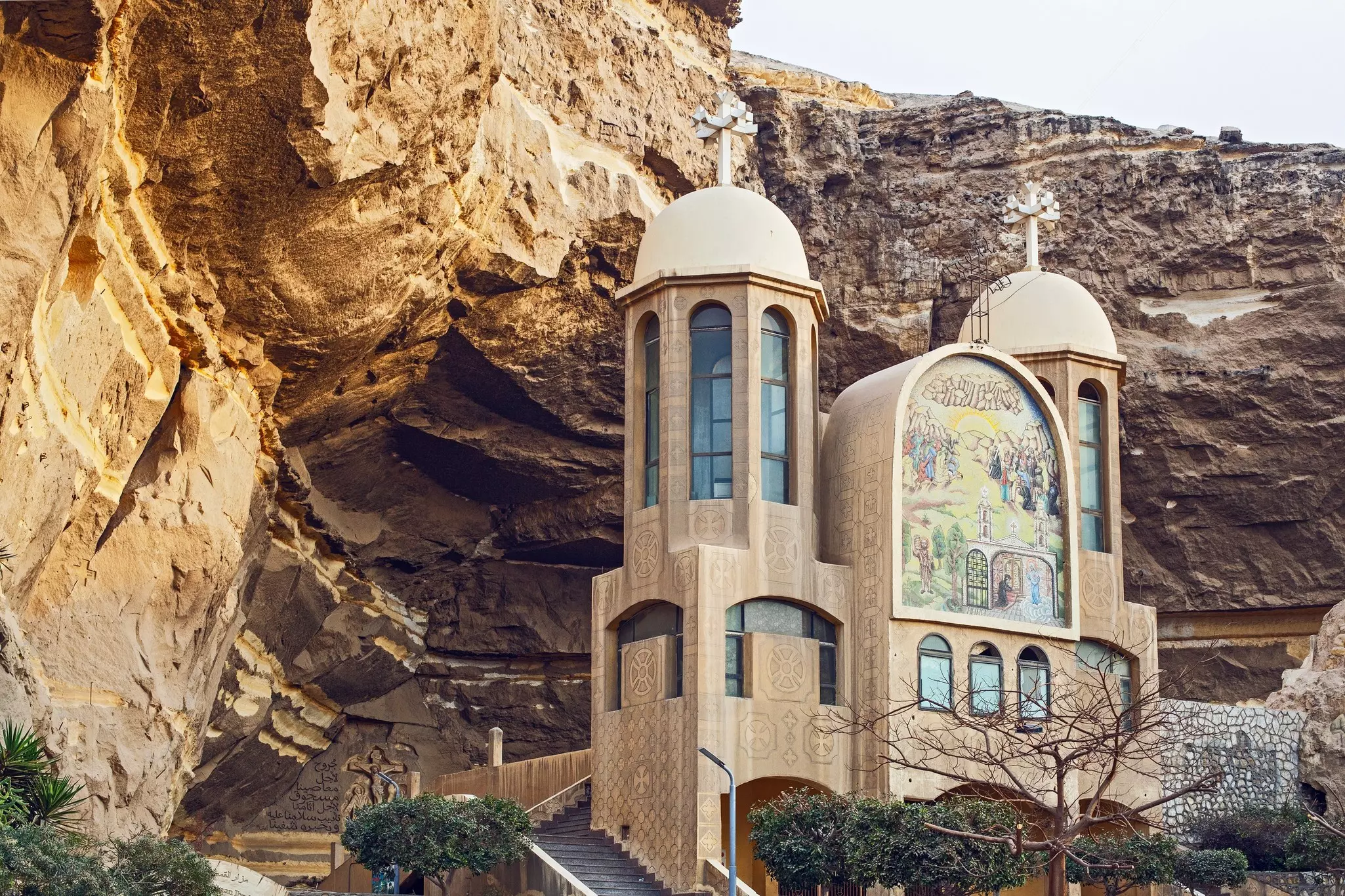 A church with two towers and a painted facade is built against a rocky cliff in Egypt.