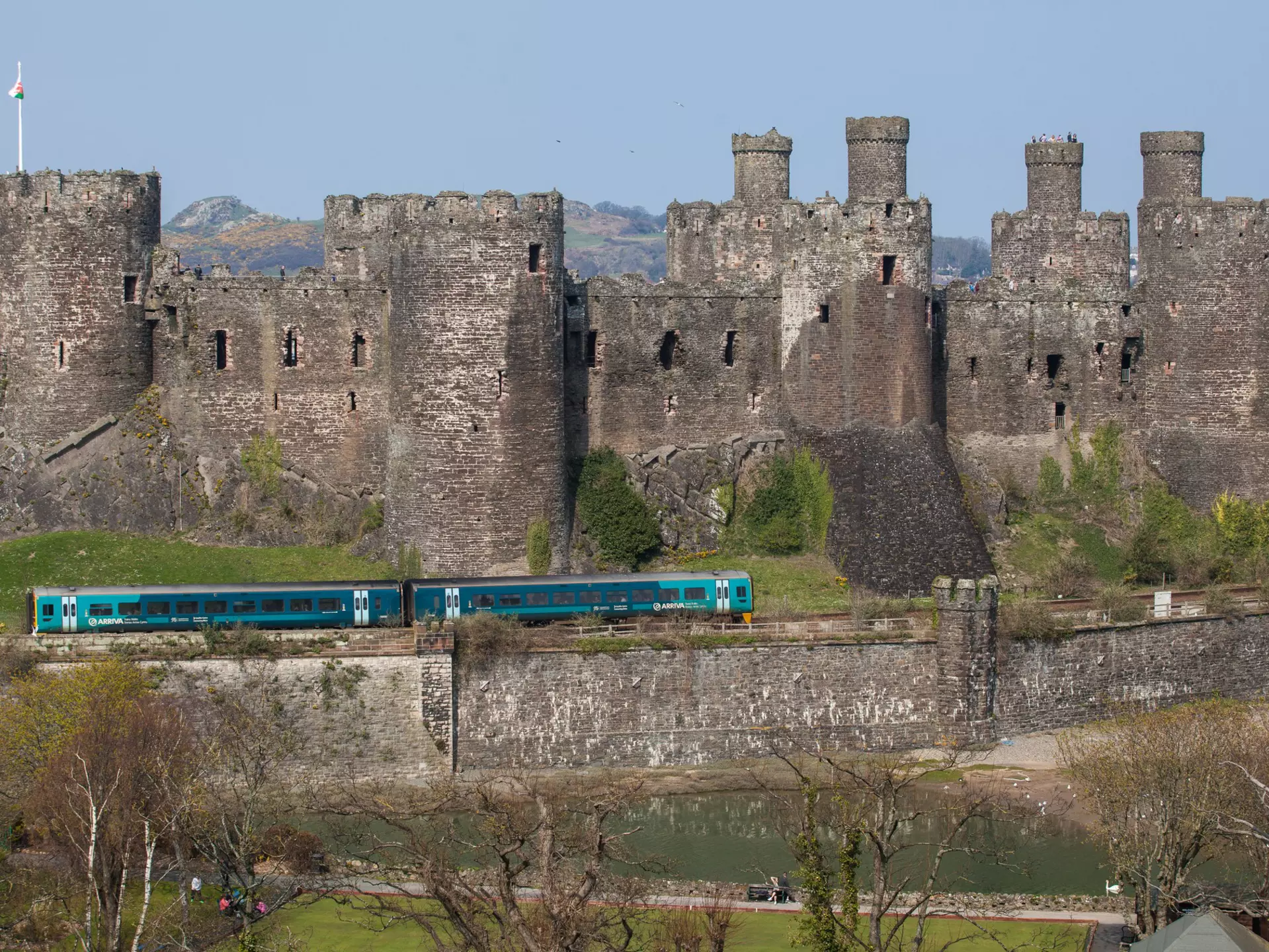 Comwy, Wales - April 9, 2015: Conwy Castle and a Passenger Train North Wales. The railway lone runs along the base of the medeval castle and the Virgin Trains service passes the castle. People can be seen on the catsle walls. The sky is clear and blue.
472088294
Surrounding Wall, Single Line, Travel, Service, People Traveling, Public Transportation, High Speed Train, Train Tunnel, Non-Urban Scene, Copy Space, Voyager, Retaining Wall, Conwy Castle, Conwy, Coastline, Caernarfon, Stone Material, Covering, Fortified Wall, Business Travel, Medieval, Blue, In A Row, Welsh Culture, Cultures, Industry, Travel Destinations, Transportation, Tourist, People, Wales, UK, Tree, Mountain Pass, Sky, Sea, Wall, Railroad Track, Castle, Passenger Train, Train, Mode of Transport, Embankment