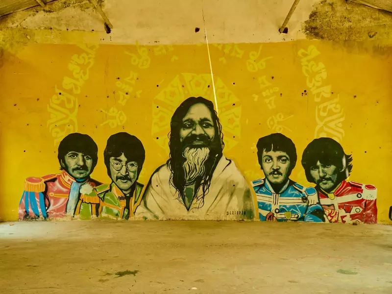 A yellow wall painted with an image of the band The Beatles surrounding famed Maharishi Mahesh Yogi