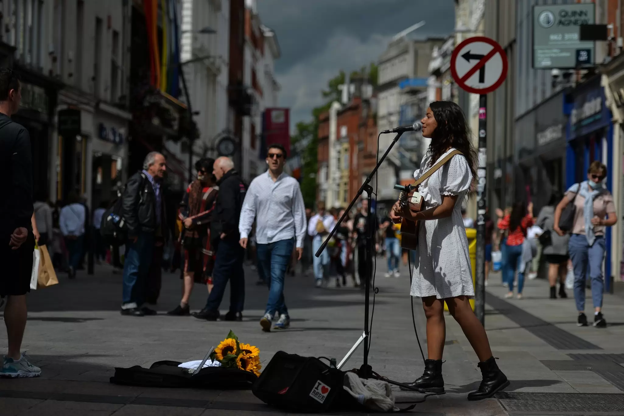 Woman in a white dress and boots playing guitar and singing on a city street in Dublin, Ireland.