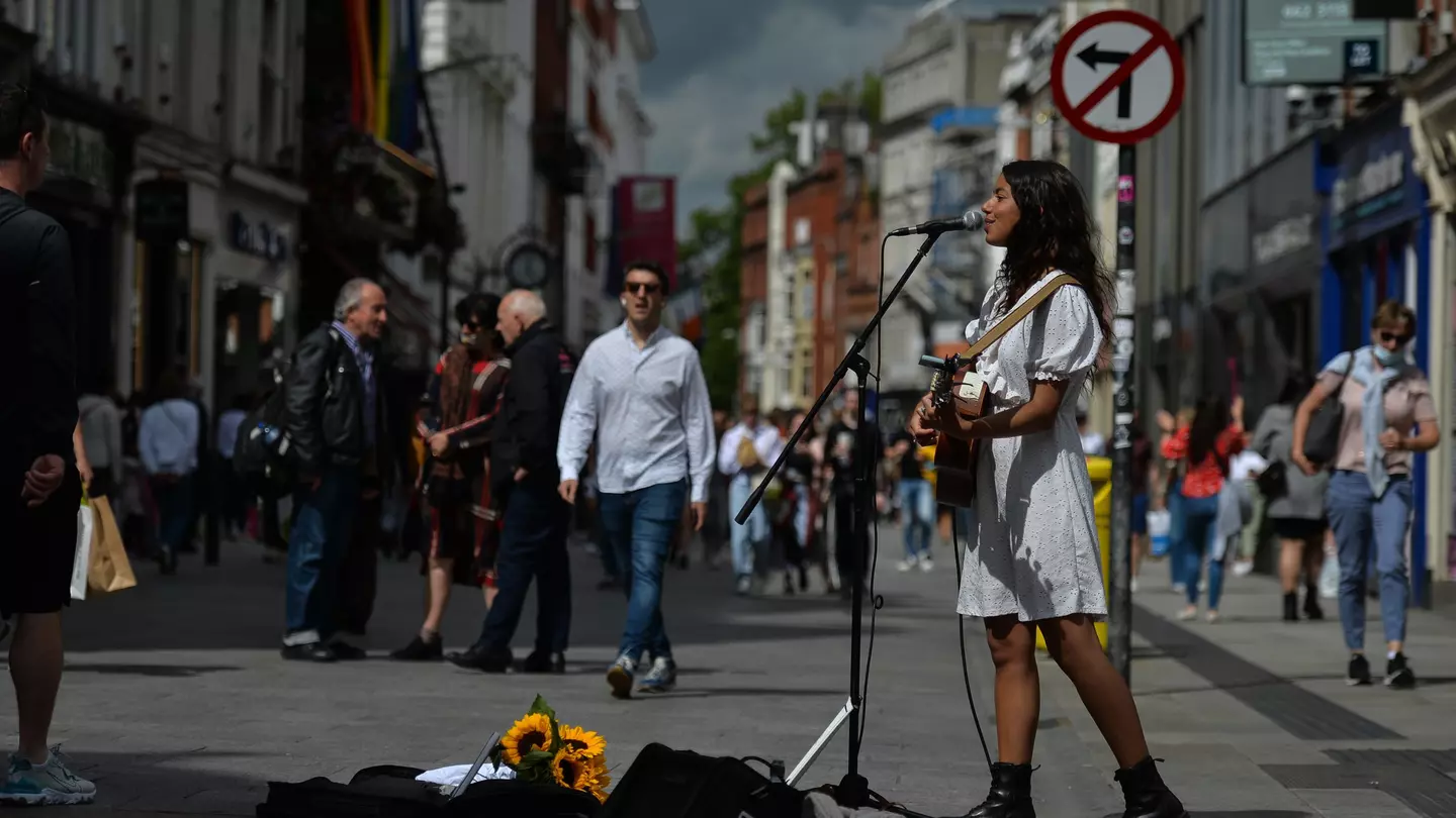 Woman in a white dress and boots playing guitar and singing on a city street in Dublin, Ireland.