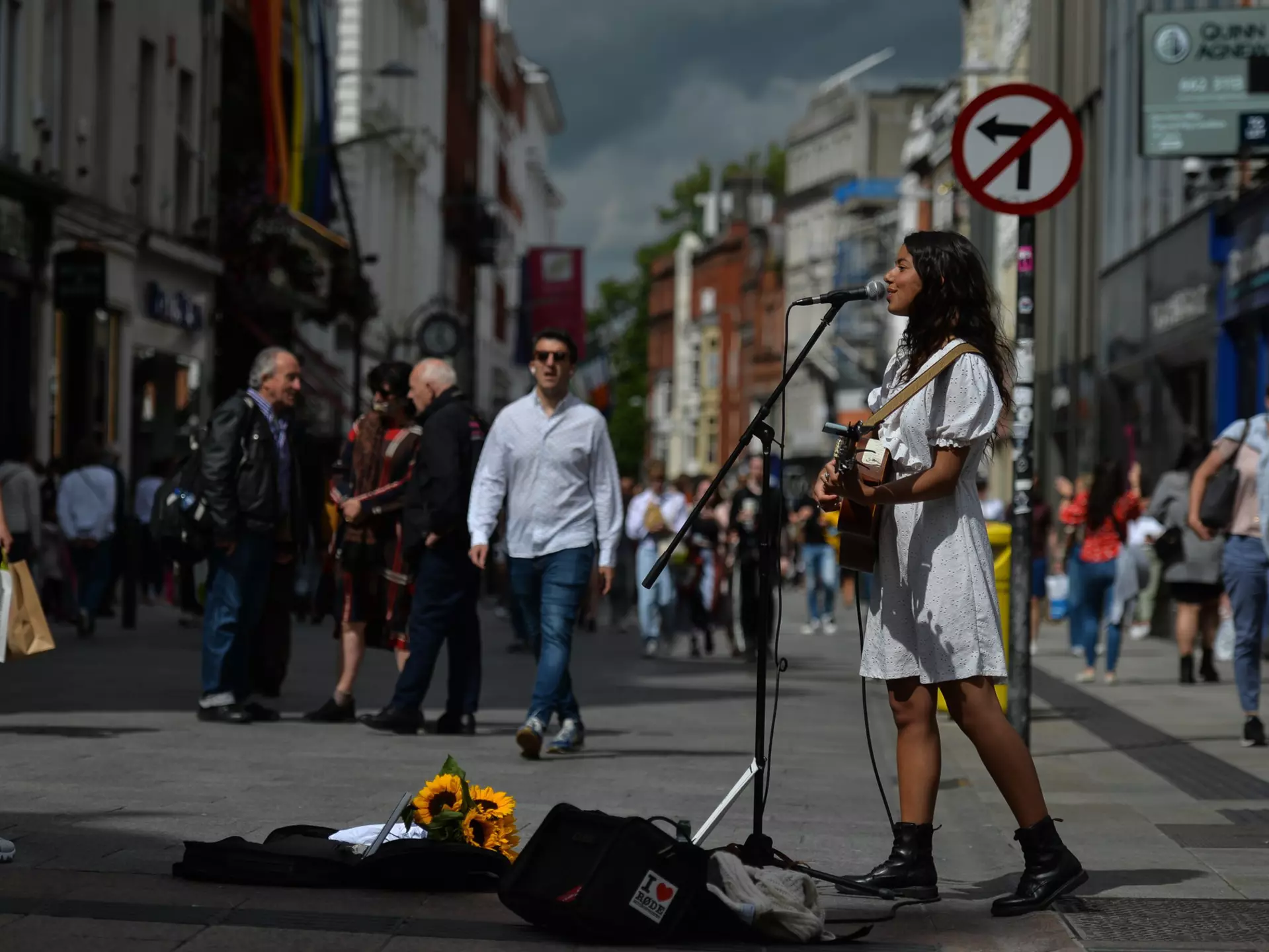 Woman in a white dress and boots playing guitar and singing on a city street in Dublin, Ireland.