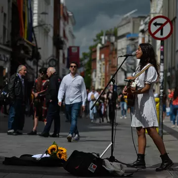 Woman in a white dress and boots playing guitar and singing on a city street in Dublin, Ireland.