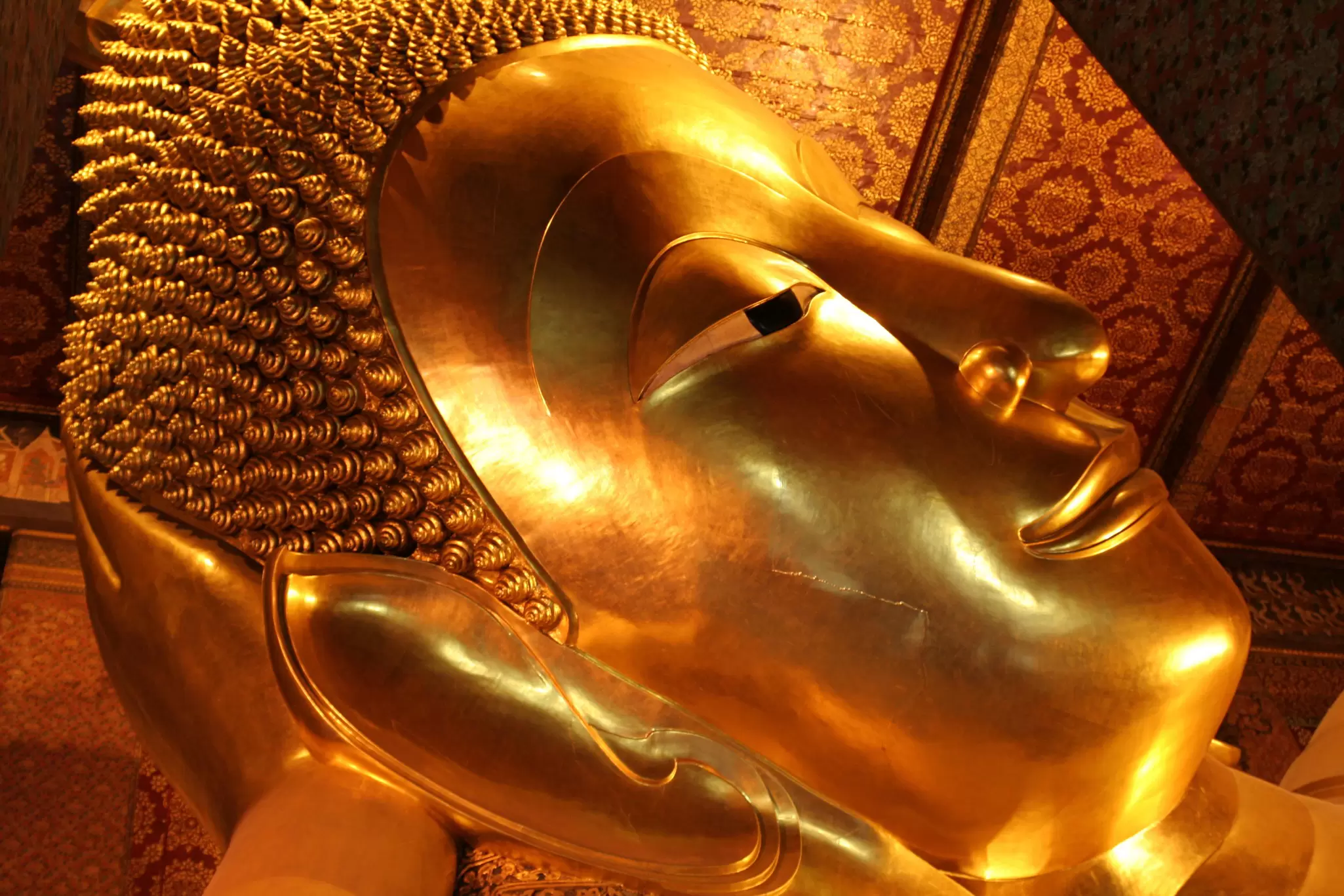 The smiling face of the massive Reclining Buddha in Bangkok in gold leaf