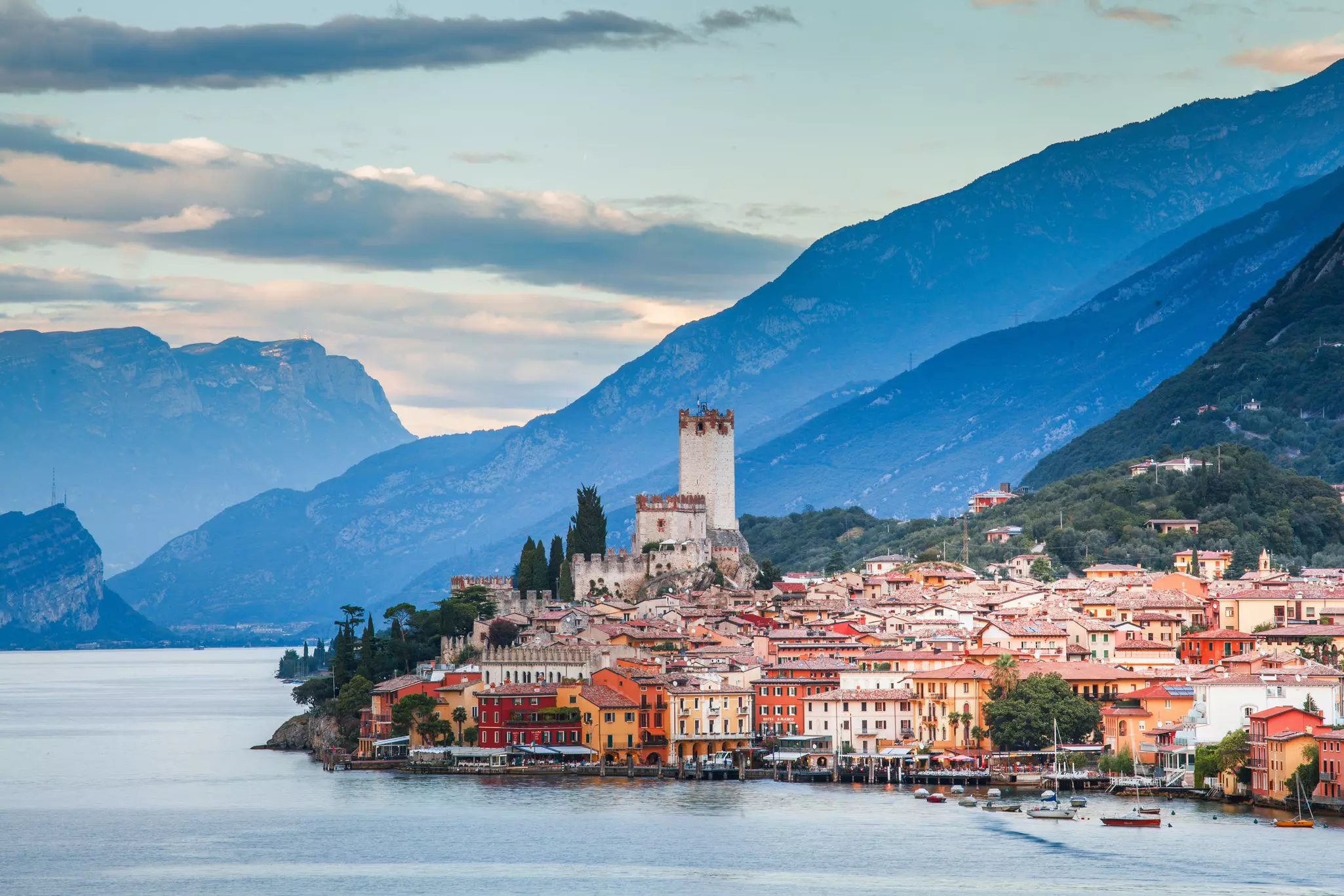 A brightly colored Italian village on the edge of a lake, with mountains in the background. 