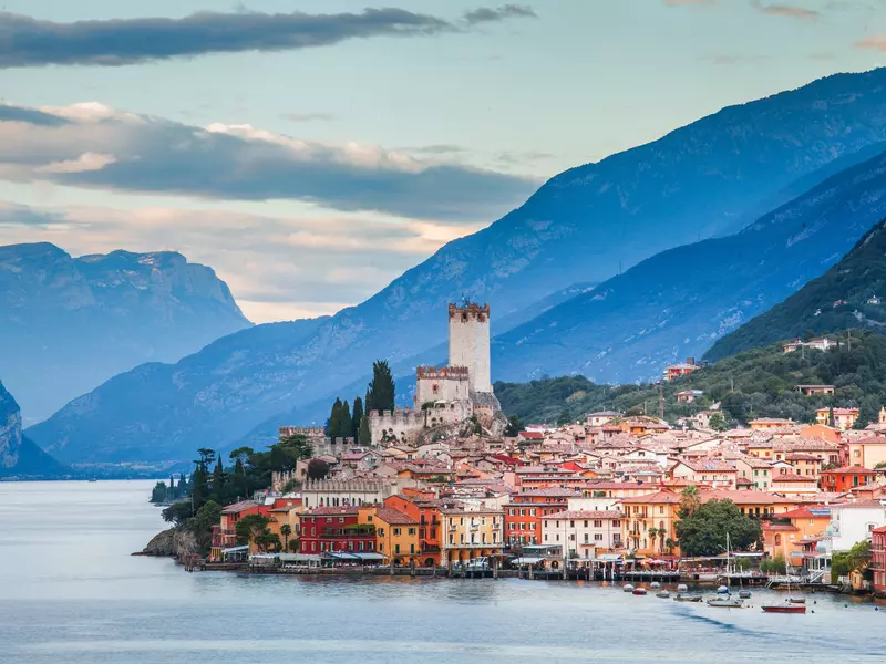 A brightly colored Italian village on the edge of a lake, with mountains in the background. 