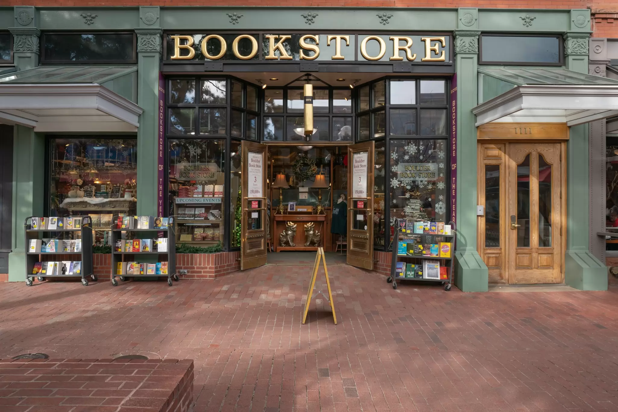 The front of a book store with books on shelves on the street outside: Boulder Bookstore, Boulder, Colorado