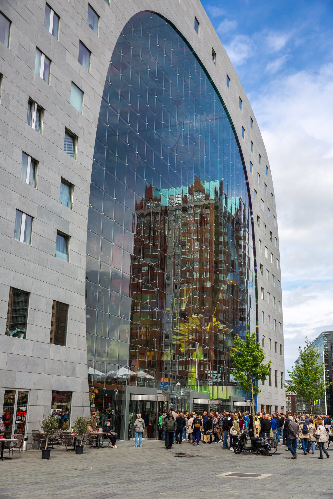Crowds gather beneath a giant glass-fronted arch on an apartment building.