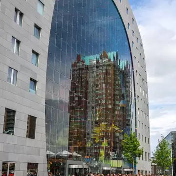 Crowds gather beneath a giant glass-fronted arch on an apartment building.