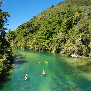 People kayak on a green river through mountains