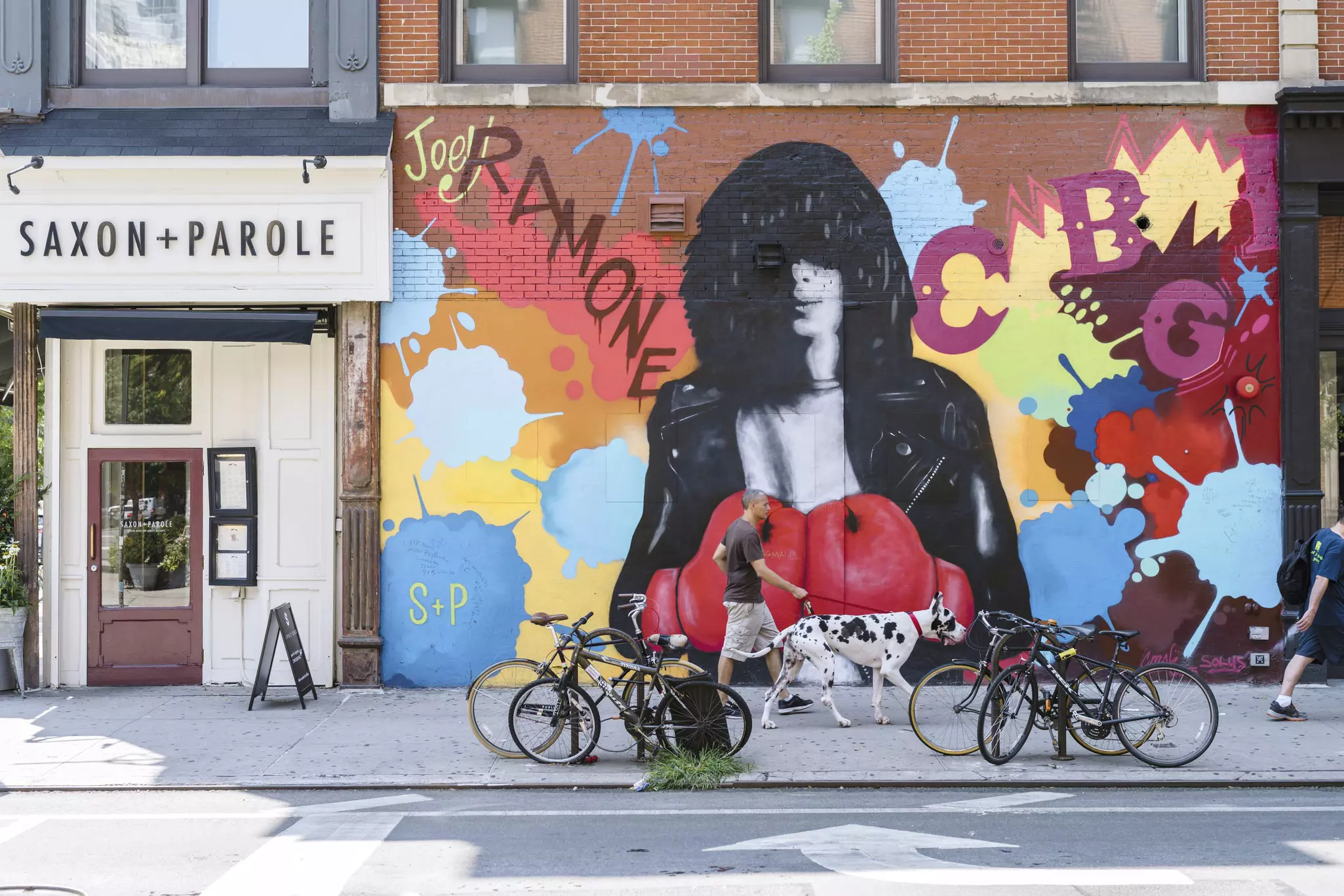 A man walks his dog in front of street art at the corner of Bleecker and Bowery in NYC.