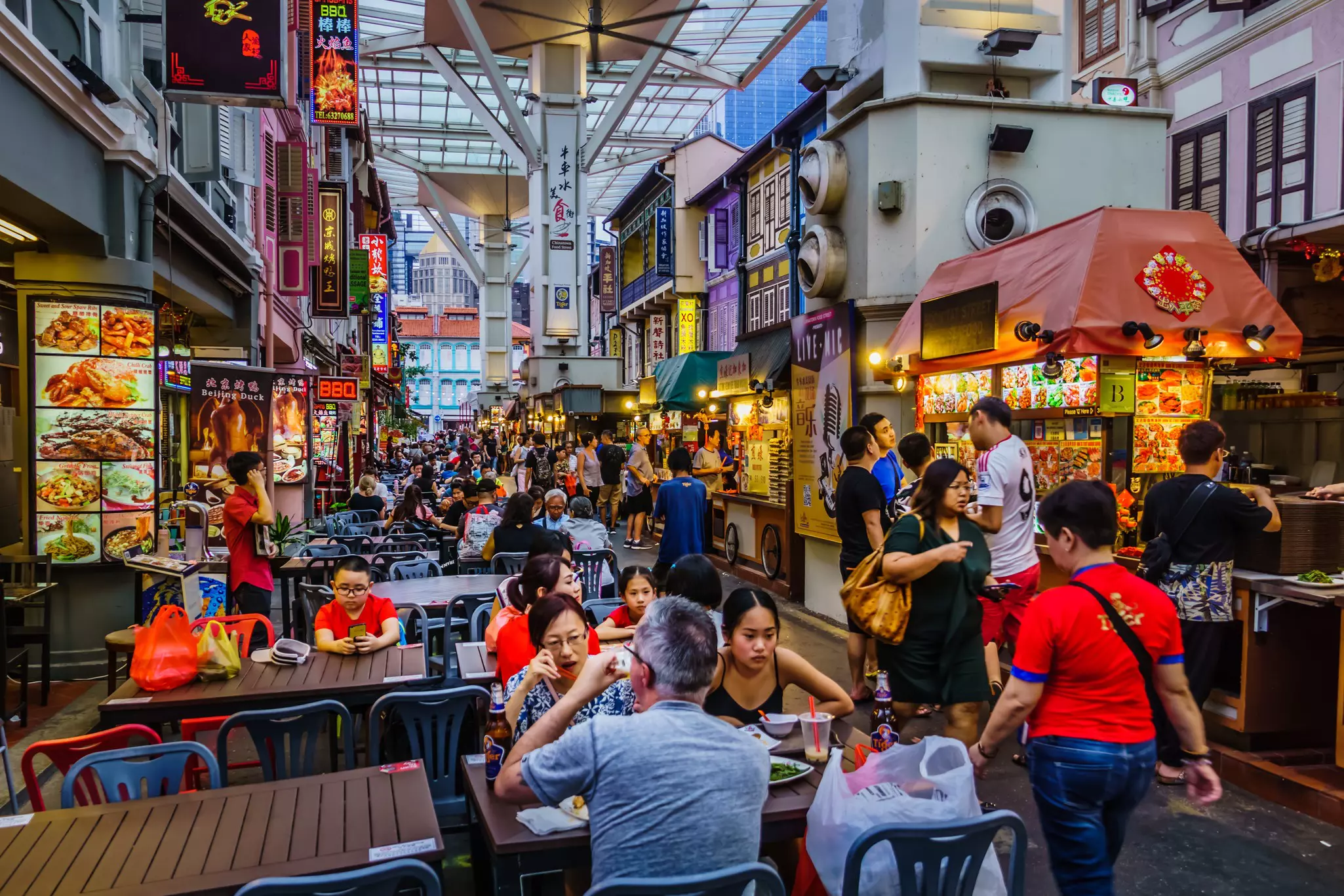 People walk by tables and food stalls in a covered food court.