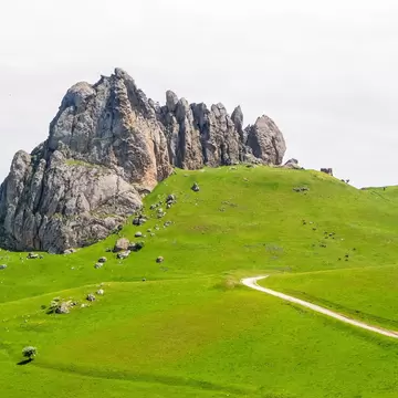 Craggy grey limestone outcrop of Beşbarmaq Dağ atop grassy slopes, with a dirt track winding below and horses grazing