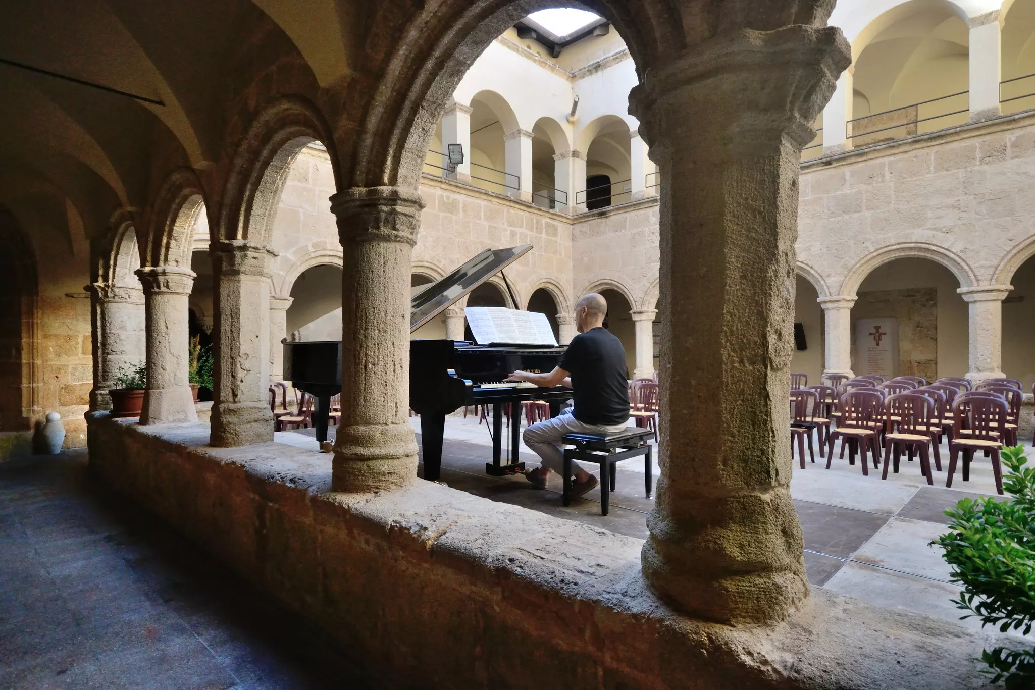 Alghero, Sardinia, Italy: Pianist plays a grand piano inside the cloister of the ancient church of San Francesco, as proof of the concert to be held in the evening