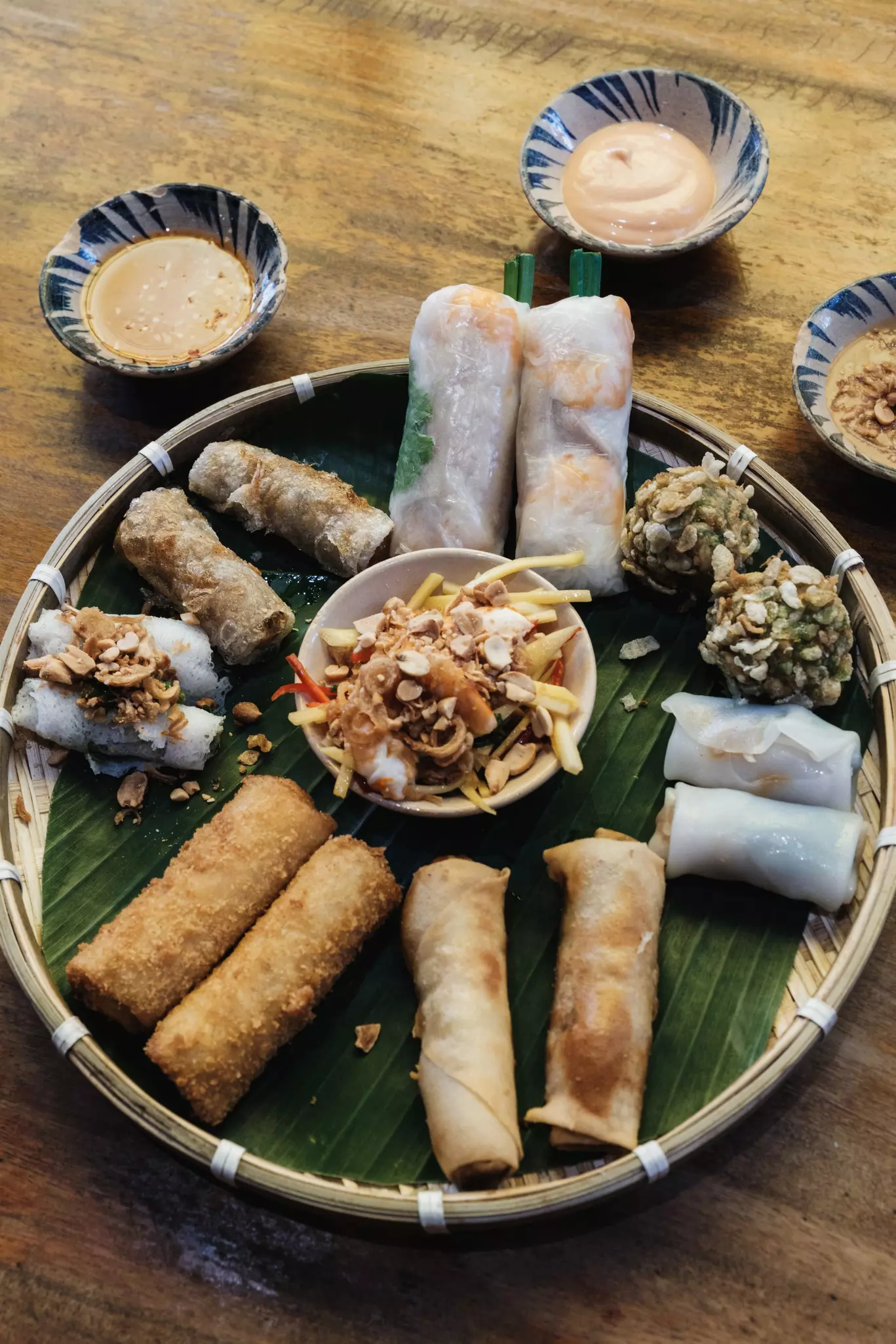 A variety of spring rolls arranged on a round bamboo tray