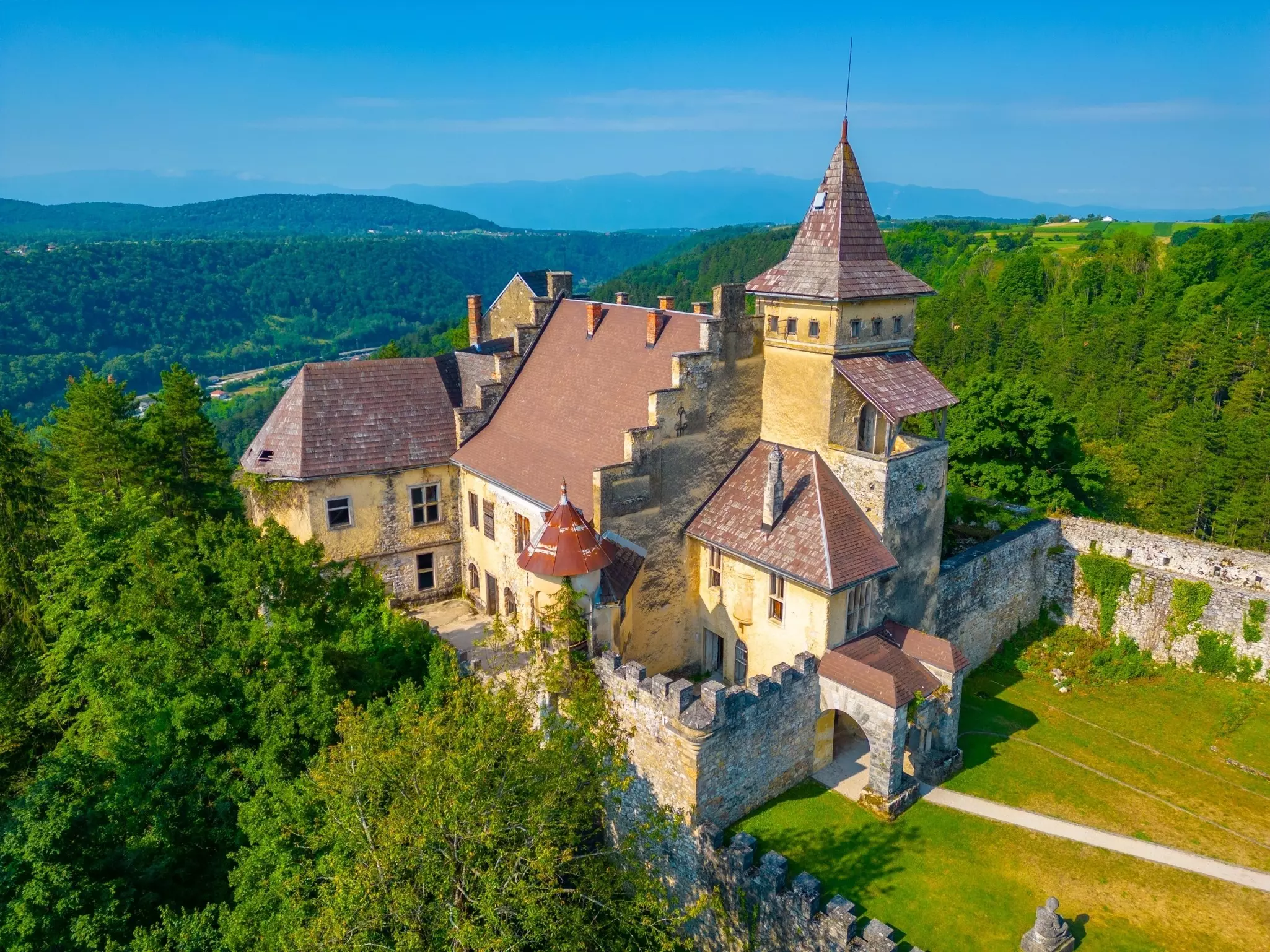 A castle high above a lush forested valley.