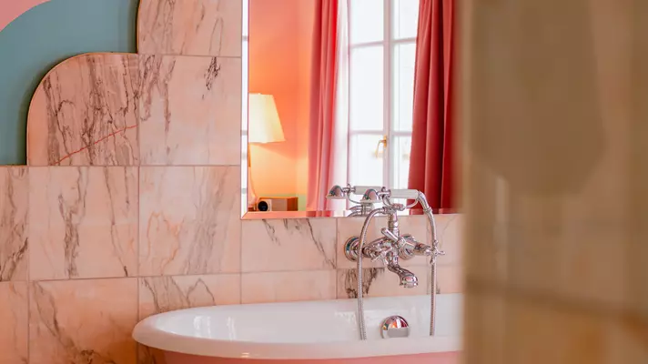 A pink claw-foot tub in a room with veined marble walls.