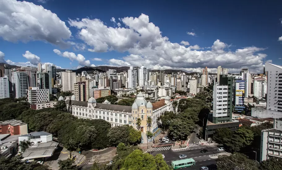 Domed historic school building amid high-rise apartments and green trees in Belo Horizonte, Brazil, with hills beyond