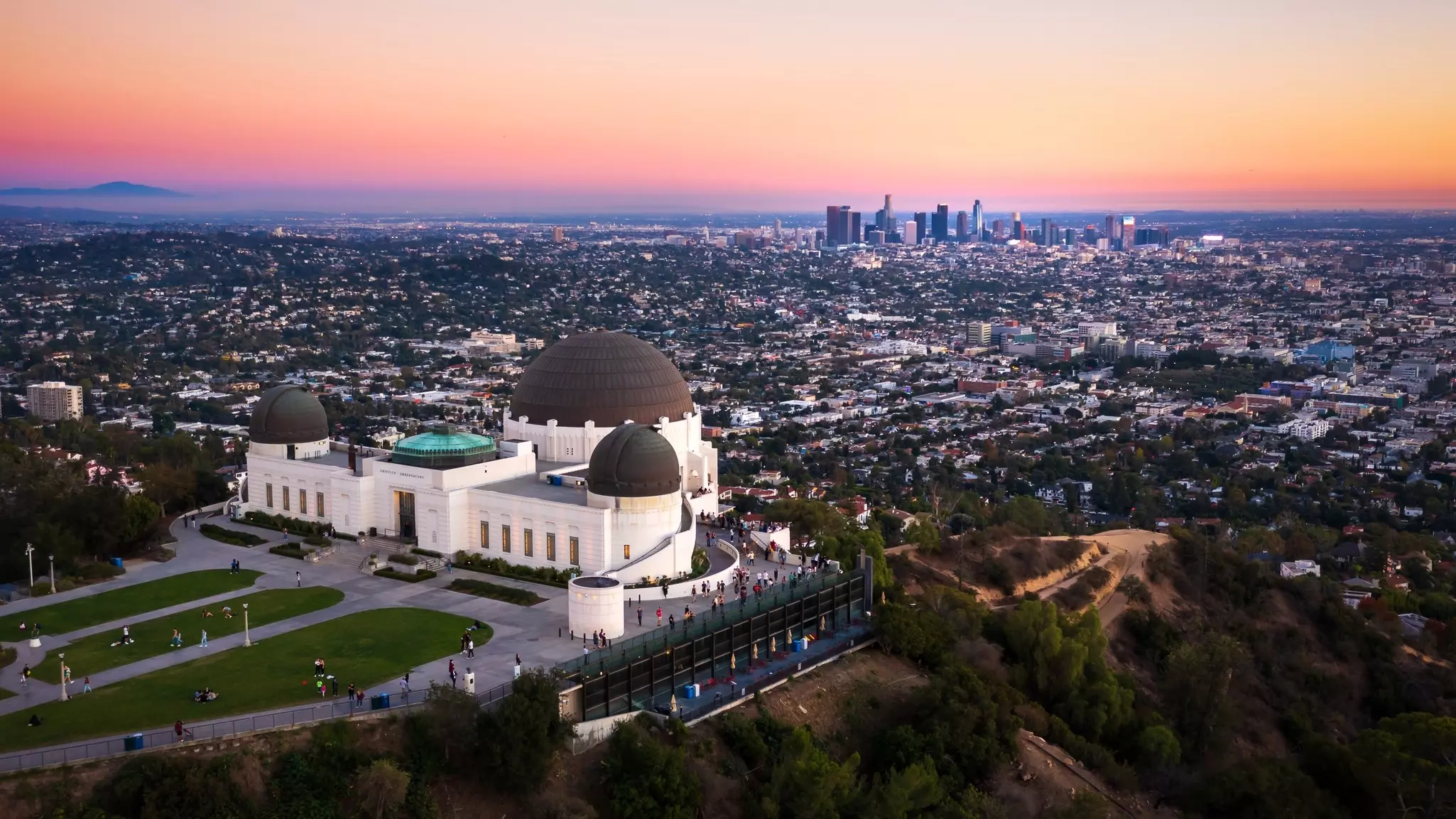 An aerial view of an art deco building on a hill overlooking a huge city, pictured at sunset.