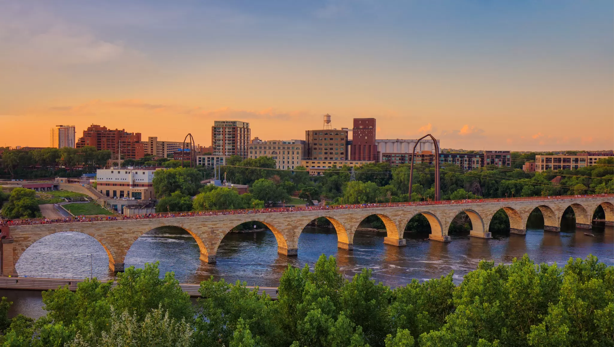 The Stone Arch Bridge crosses the Mississippi River in Minneapolis, backed by the sunset.