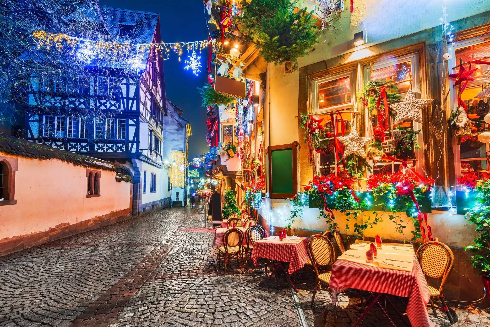 A cobbled street and restaurant with Christmas lights and decorations on a winter's evening.