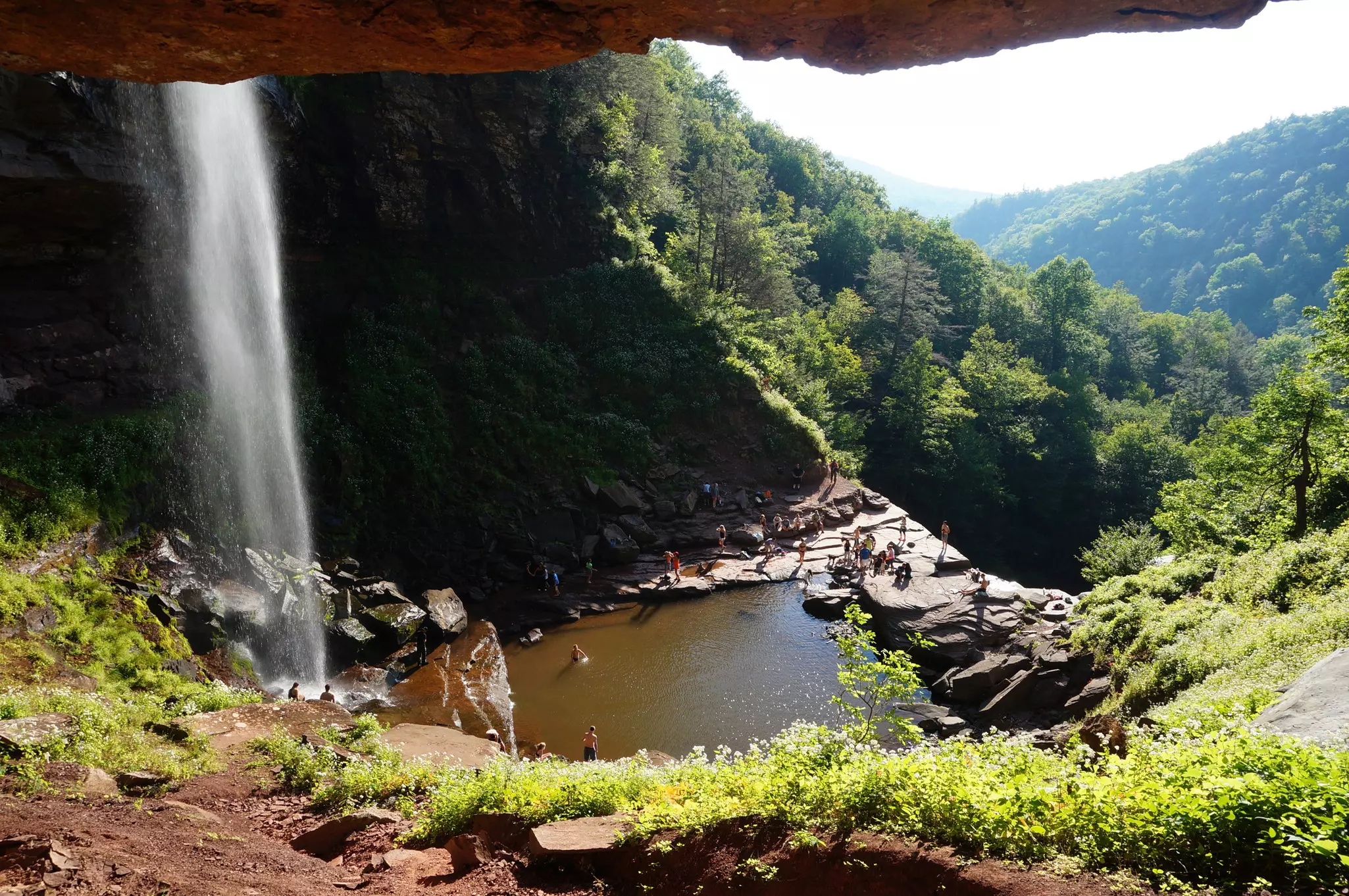 A wide view of a waterfall pouring into a pool cut into a mountainside. Swimmers are seen in the pool below.