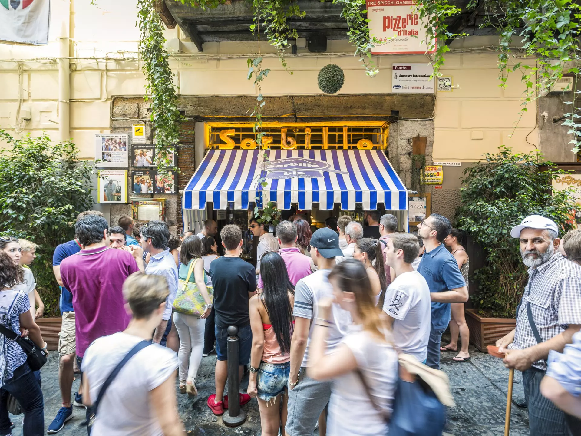 People crowded outside a storefront with blue and white awning that says "Sorbillo"