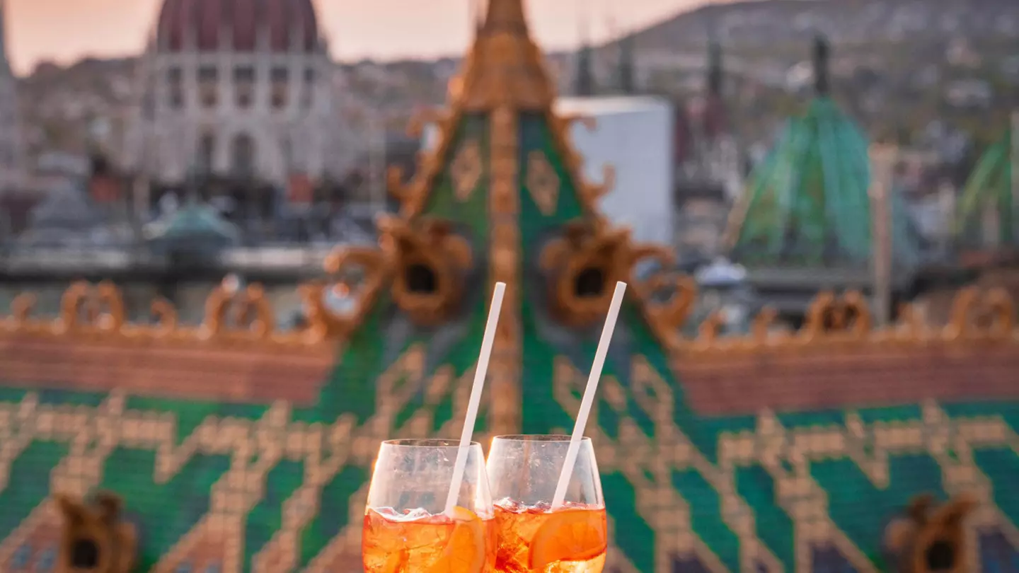 A pair of cocktails at sunset on a rooftop ledge in focus, with buildings including the Parliament in the background, Budapest, Hungary, Europe