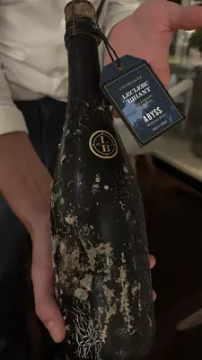 A hand holding a dark bottle of champagne labeled "Leclerc Briant"