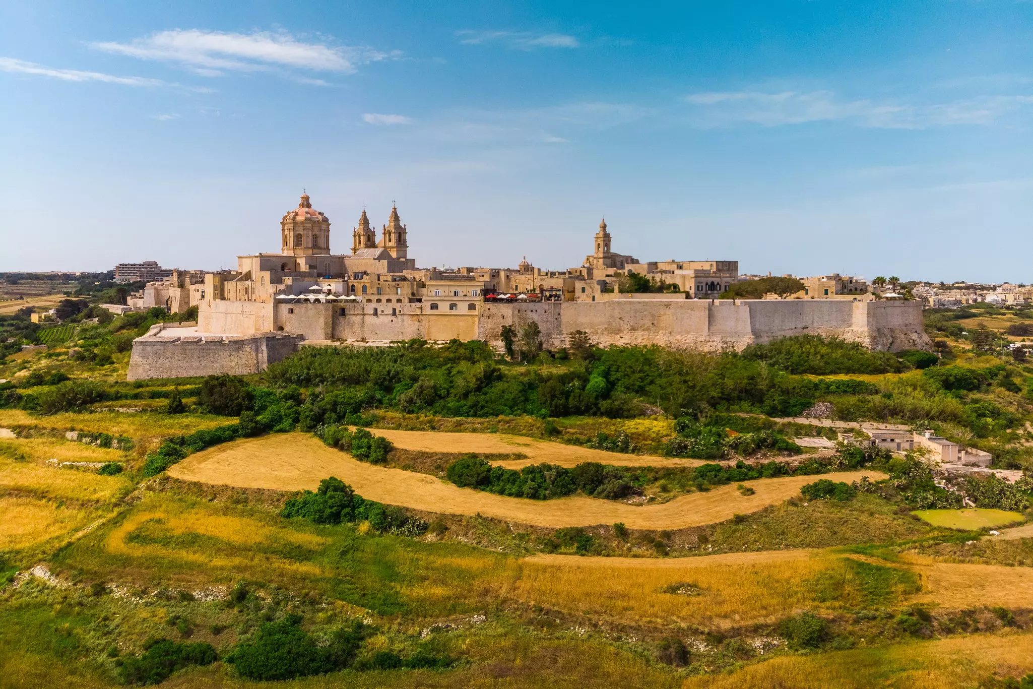 A large walled citadel among fields bathed in sunshine.