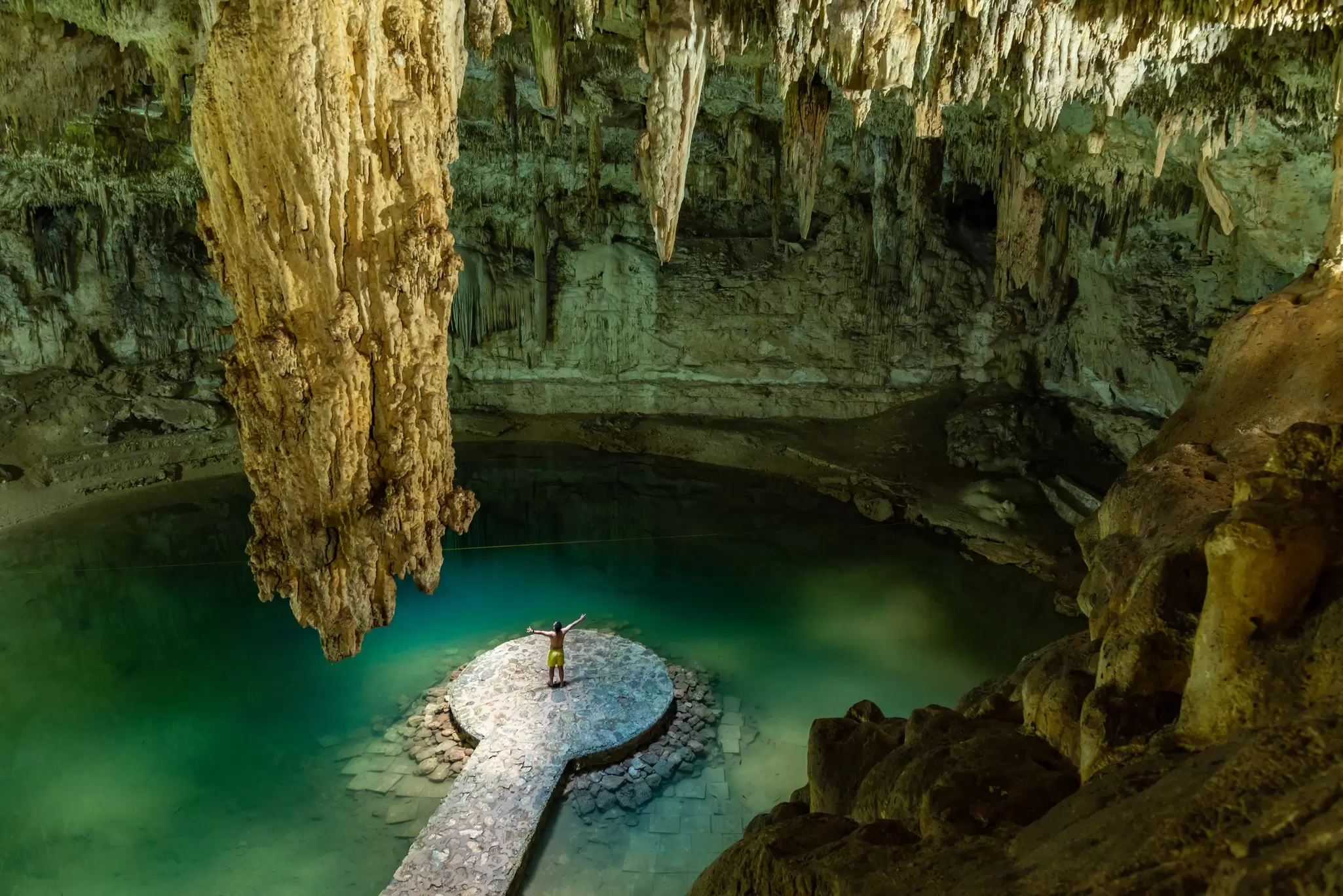 An overhead view of a man raising his arms on a platform in a large underground pool with huge stalactites above, Cenote Suytun, near Valladolid, Yucatán Peninsula