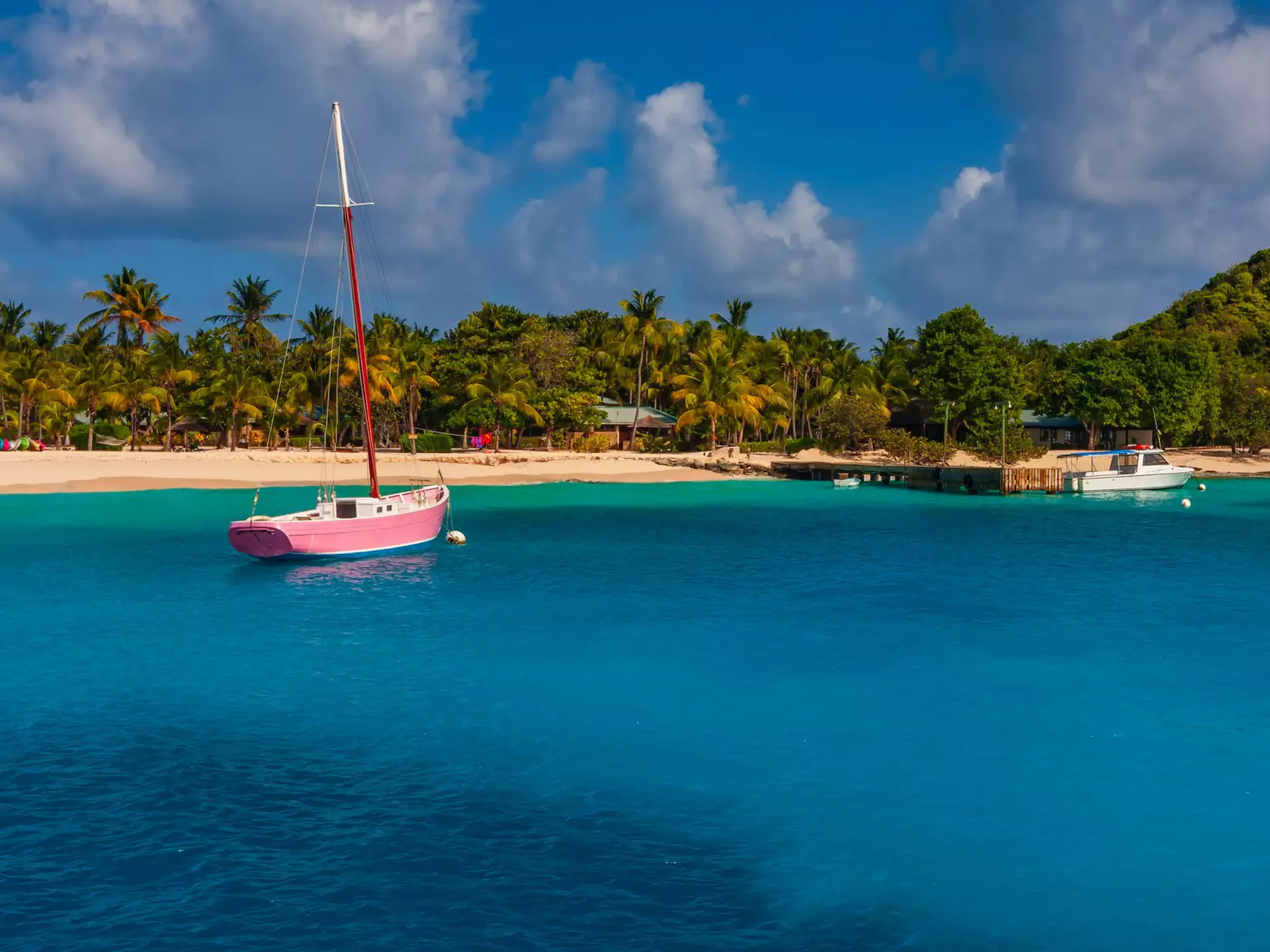 A pink boat is docked in blue water off a sandy beach.