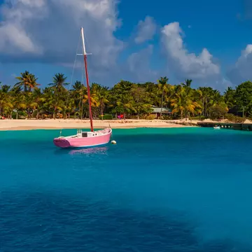 A pink boat is docked in blue water off a sandy beach.